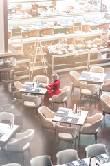Portrait of gorgeous lady with blonde hair wearing red jumpsuit, looking at the screen of her laptop while sitting in an empty restaurant. Successful beautiful woman concept. Vertical shot. Top view