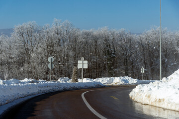 Snowy road scene in winter, with snowy trees, rocks and asphalt road.