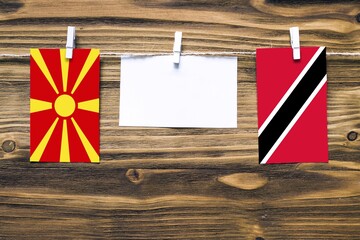 Hanging flags of Macedonia and Trinidad And Tobago attached to rope with clothes pins with copy space on white note paper on wooden background.Diplomatic relations between countries.