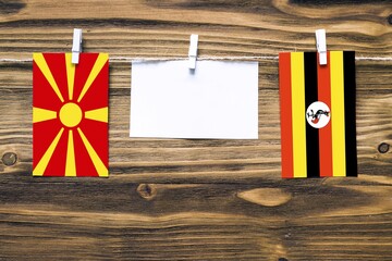 Hanging flags of Macedonia and Uganda attached to rope with clothes pins with copy space on white note paper on wooden background.Diplomatic relations between countries.