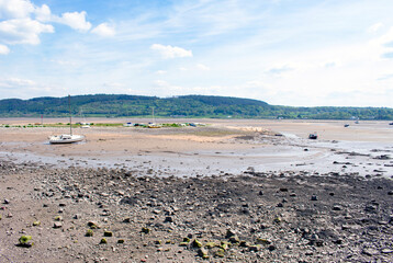 The tide is out a Red Wharf bay on the island of Anglesey. Sand flats and show how shallow the Irish sea is at this point. Boats rest on the sands. Green hills form the backdrop.