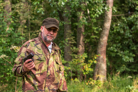 Old bearded thug with a gun in his hand. Russian gangster in camouflage uniform in the forest. Forest brother with a gun