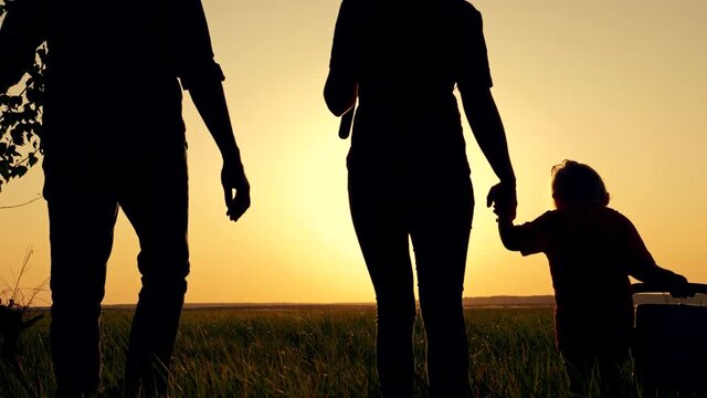 Happy, close-knit family with children, silhouette of farmers outdoors holding hands at sunset. Dad holds a young tree in his hand. The way of life in rural areas.