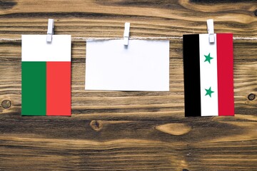 Hanging flags of Madagascar and Syria attached to rope with clothes pins with copy space on white...