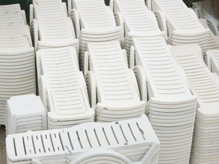 Plastic white chaise lounges stacked in a pile on the resort storage after a hot season. Leisure or travel concept. Pile of white plastic sunbeds, deck chairs 