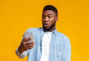 Surprised african man looking at smartphone screen with mouth opened