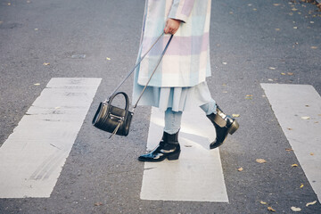 fashion blogger street style. fashionable woman posing wearing oversized checked coat, black ankle boots and a black trendy mini handbag. crossing the street. detail of a perfect fall 2019 outfit.  - Powered by Adobe