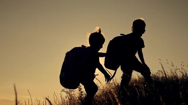 Two little tourist kids travel with backpacks on their backs. Silhouette of happy children boy and girl at sunset.