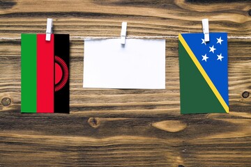 Hanging flags of Malawi and Solomon Islands attached to rope with clothes pins with copy space on...