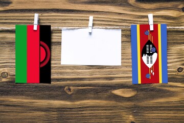 Hanging flags of Malawi and Swaziland attached to rope with clothes pins with copy space on white...