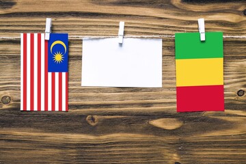 Hanging flags of Malaysia and Mali attached to rope with clothes pins with copy space on white note paper on wooden background.Diplomatic relations between countries.