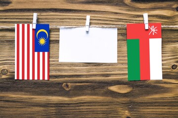 Hanging flags of Malaysia and Oman attached to rope with clothes pins with copy space on white note paper on wooden background.Diplomatic relations between countries.