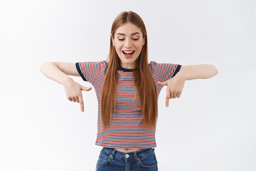 Intrigued, excited good-looking woman with fair hair, wear striped t-shirt, pointing looking down...