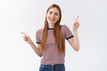 Friendly, pleasant cheerful woman in striped t-shirt with long fair hair, raise hands pointing...