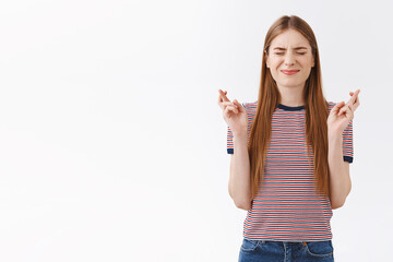 Nervous cute good-looking girl with long fair hair, wear striped t-shirt, smirk and shut eyes as cross fingers for good luck, praying dream come true, standing intense anticipating hopefully