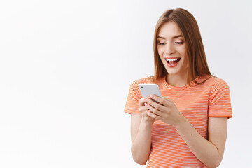 Surprised, enthusiastic pretty young woman in striped t-shirt, hold smartphone read amazing news, open mouth fascinated, smiling react to wonderful prices on mobile app shopping site