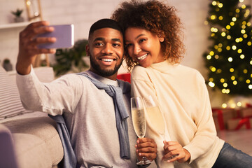 Christmas time. Afro couple taking selfie against xmas tree