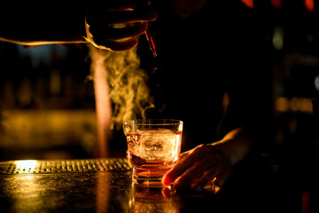 Professional bartender drop an essence to a a glass with cocktail with ice