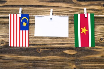 Hanging flags of Malaysia and Suriname attached to rope with clothes pins with copy space on white...