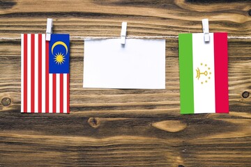 Hanging flags of Malaysia and Tajikistan attached to rope with clothes pins with copy space on white note paper on wooden background.Diplomatic relations between countries.
