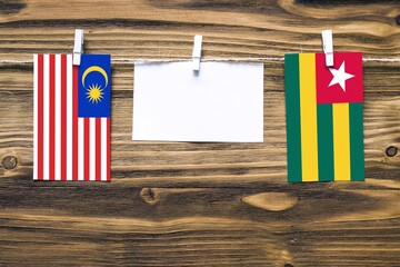 Hanging flags of Malaysia and Togo attached to rope with clothes pins with copy space on white note paper on wooden background.Diplomatic relations between countries.