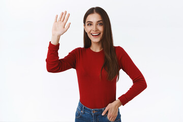Friendly, enthusiastic good-looking brunette female student in red sweater, raising hand up in...