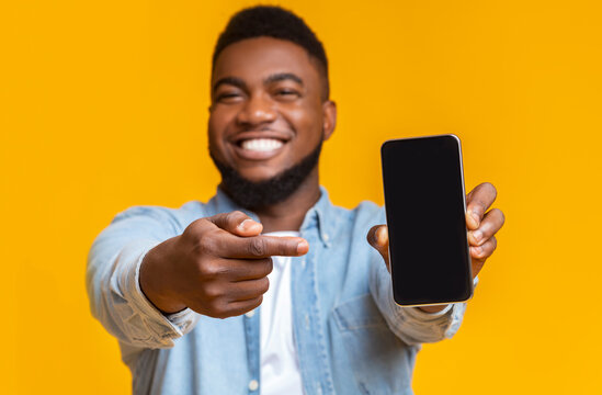 Cheerful african guy pointing at smartphone with black screen