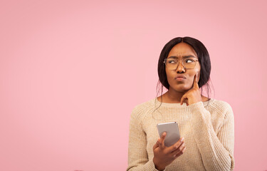 Pensive Afro Girl Holding Cellphone Thinking Standing On Pink Background