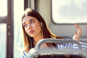 Close-up portrait of lonely female travels in bus trip, wistfully looking at window and listening...