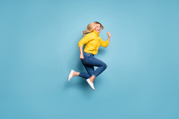 Fototapeta na wymiar Full length photo of pretty blond lady jumping high rushing mall discounts low prices shopping wear knitted yellow pullover jeans isolated blue color background
