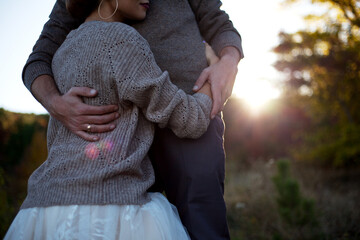 close-up of happiness wedding couple wearing sweater, dress and suit, resting in the nature. The groom hug the bride with love against the beautiful vie of the sun and leaves.
