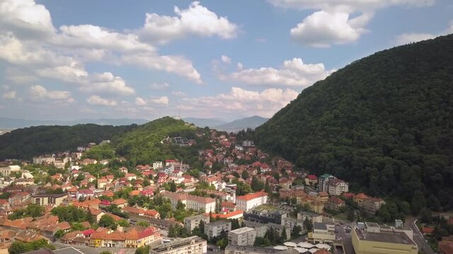 Aerial view of Brasov city, medieval town situated in Transylvania, Romania. Old architecture surrounded with big Carpathian mountains covered with dense green forest.