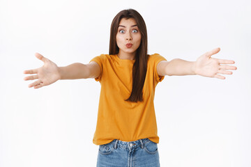 Silly cute good-looking european woman in yellow t-shirt, spread hands sideways and folding lips in kiss, waiting someone fall into her arms to cuddle, hug, standing flirty over white background