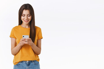 Attractive, carefree emotive young brunette woman in yellow t-shirt, holding smartphone smiling...
