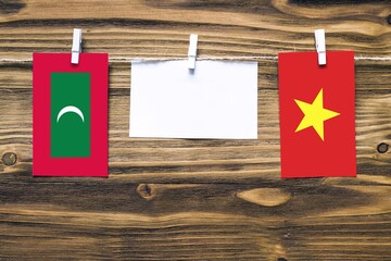 Hanging flags of Maldives and Vietnam attached to rope with clothes pins with copy space on white note paper on wooden background.Diplomatic relations between countries.