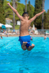 European boy in blue swimming shorts is diving to the swimming pool. He is enjoying his summer holidays in Spain.