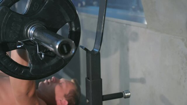 Professional athletic man bodybuilder doing barbell chest exercise on bench, closeup view. Man pumping chest with naked torso. Perfect bench press technique. White smoke in gym in dark.