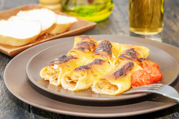 Fototapeta premium Cooked hot stuffed cannelloni for eating on the natural wooden table.