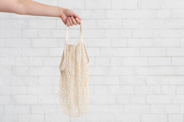 Woman holding empty eco net bag over white bricks wall