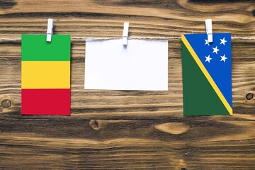 Hanging flags of Mali and Solomon Islands attached to rope with clothes pins with copy space on...
