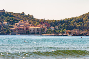 Man swimming in the sea with the landscape cityscape view of the Poggio Pertuso in the front of the Tenda Gialla beach in Province of Grosseto, Tuscany on the background