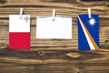 Hanging flags of Malta and Marshall Islands attached to rope with clothes pins with copy space on white note paper on wooden background.Diplomatic relations between countries.