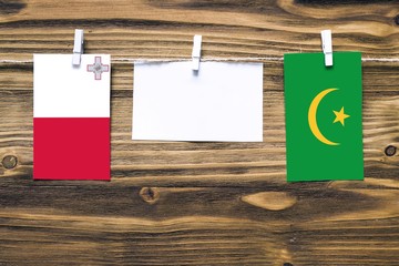 Hanging flags of Malta and Mauritania attached to rope with clothes pins with copy space on white note paper on wooden background.Diplomatic relations between countries.