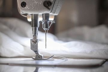 Needle of white industrial sewing machine use sew white cloth close-up.