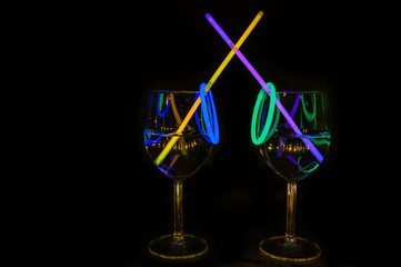 Cocktail wine glass filled with exotic illuminated refreshing alcohol liquid and colorful straw with black background for nightlife party