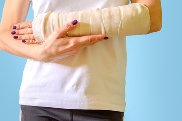 Woman with broken arm bone in cast, plastered hand on blue background. Close up.