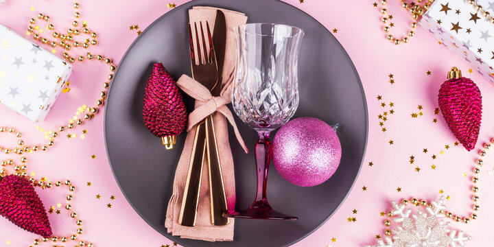 Christmas festive dinner tableware, golden ornament. Flat lay on pink background with star confetti.