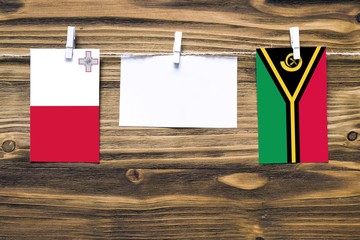 Hanging flags of Malta and Vanuatu attached to rope with clothes pins with copy space on white note...