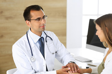 Doctor reassuring her female patient because of her first pregnancy fear while sitting at a desk in...