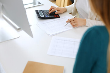 Accountant checking financial statement or counting by calculator income for tax form, hands close-up. Business woman sitting and working with colleague at the desk in office. Audit concept